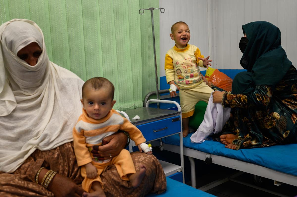 A la derecha, una madre de 22 años ríe con su hijo de 2 años que sufre desnutrición grave y neumonía, mientras que, a la derecha, su hijo de 7 meses, que sufre desnutrición grave y también está enfermo, se sienta en el regazo de su suegra. Ambos niños reciben tratamiento en una sala de hospitalización de la unidad de alimentación terapéutica de Acción contra el Hambre en la zona de Ahmad Shah Baba Mina, en Kabul, el 15 de abril de 2023