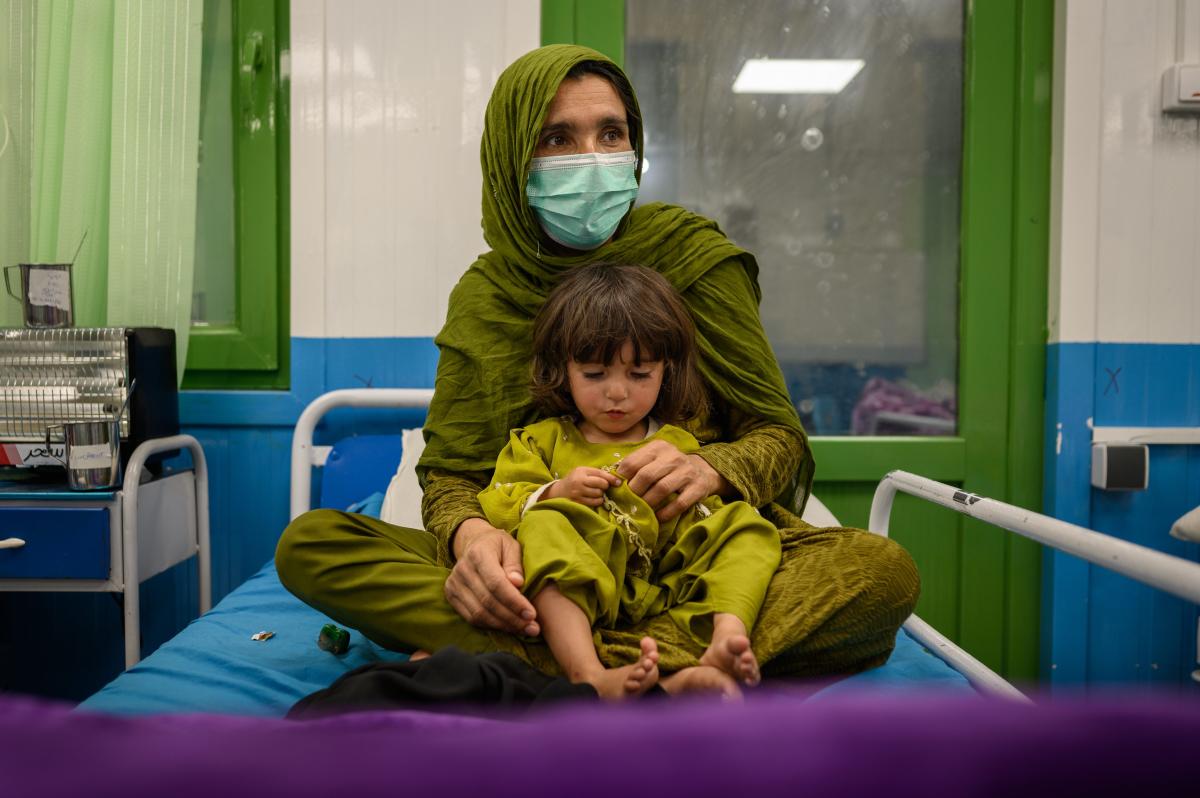 Una madre sentada con su hija de 4 años, desnutrida y enferma la noche anterior, en una sala de hospitalización de la unidad de alimentación terapéutica de Acción contra el Hambre en la zona de Ahmad Shah Baba Mina, en Kabul, el 15 de abril de 2023 (Foto de Elise Blanchard para Acción contra el Hambre).