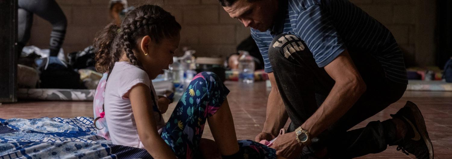 Un hombre ata los cordones de sus hijas, con las que ha pasado la noche en un albergue para migrantes