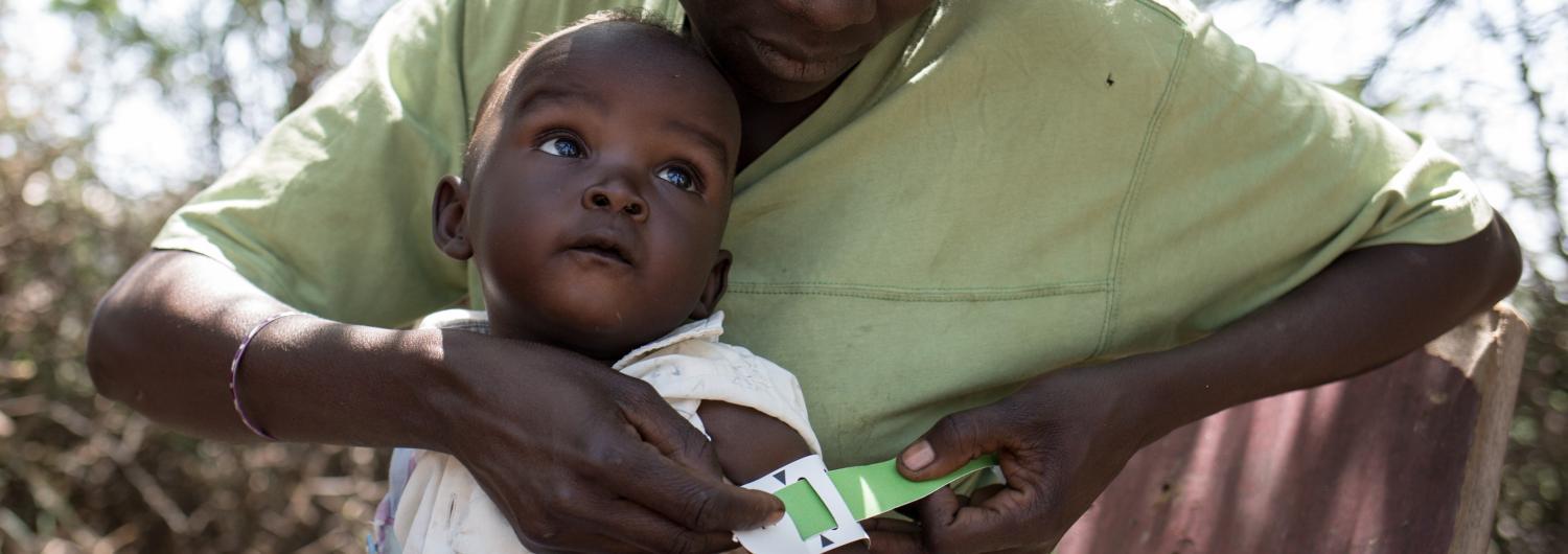 A woman measures the degree of malnutrition of a child with a MUAC tape. 