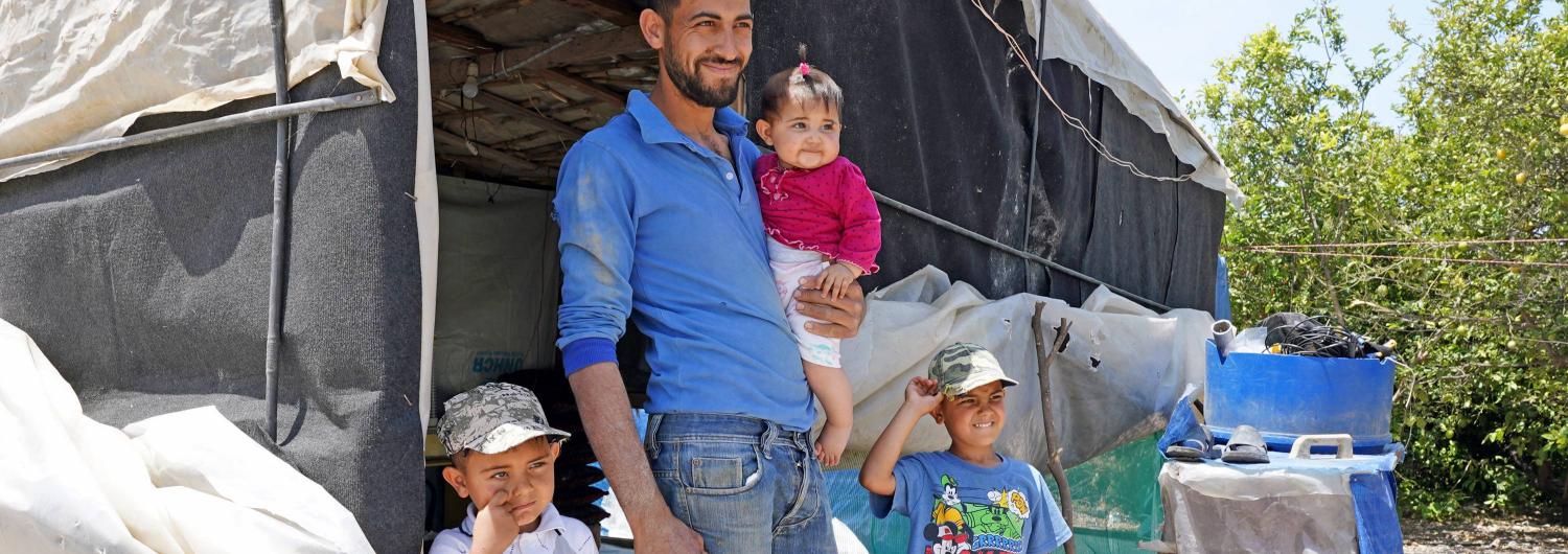 un padre refugiado sirio junto a sus tres hijos frente a una tienda en el Líbano