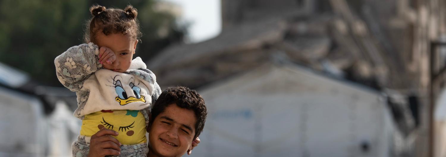 Ahmed, de ocho años, uno de los niños que viven en una escuela reconvertida en refugio para las víctimas del terremoto gracias a la ayuda de Acción contra el Hambre, lleva a su hermana pequeña en el patio del refugio en Aleppo © Hasan Belal para DEC y Acc