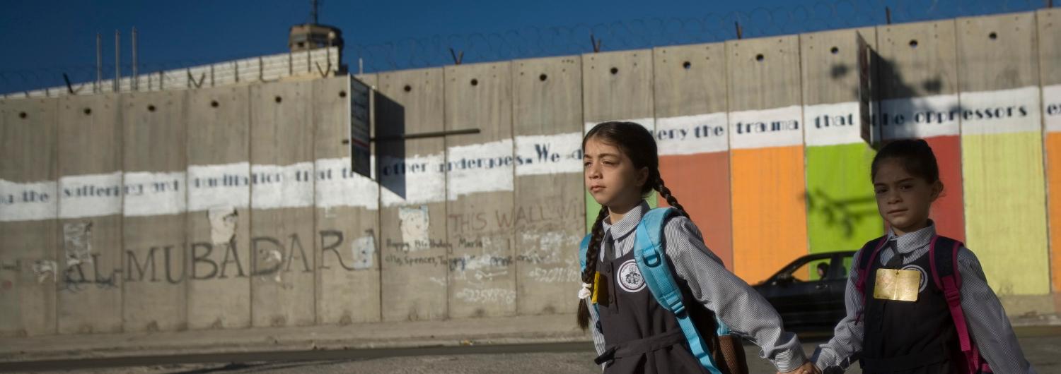 Dos niñas palestinas van de la mano al colegio junto al muro de anexión y separación construido por el gobierno israelí en Cisjordania